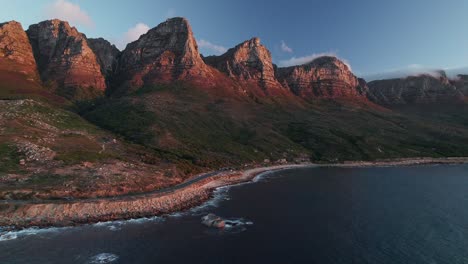 Victoria-Road-Con-Las-Montañas-De-Los-Doce-Apóstoles-En-Ciudad-Del-Cabo,-Sudáfrica---Toma-Aérea-De-Un-Drone