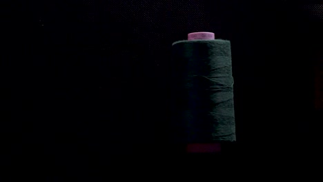 thread-spool-on-bobbin-roll-color-on-black-background-slow-motion