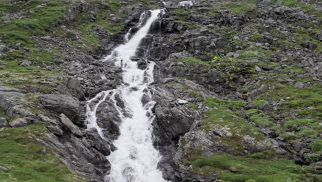 Aerial-dolly-shot,-pulling-back-from-a-narrow-river-as-it-winds-down-a-steep,-rocky,-mossy-hillside,-near-the-Trollstigen,-Norway