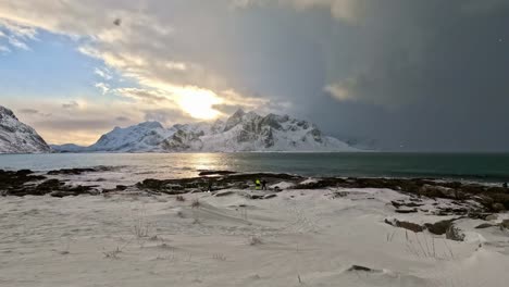 Persons-at-beach-experience-arrival-of-snow-and-dark-skies-in-Vareid-and-Flakstad,-Norway