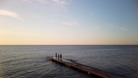 Kids-swim-and-climb-up-on-ladder-on-jetty-by-open-ocean-at-sunset