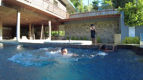 Kids-playing-by-the-swimming-pool-by-pushing-each-other-and-falling-into-the-water,-dynamic-handheld