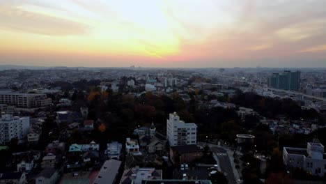 Paisaje-Urbano-Al-Atardecer-Con-Cielos-Vivos-Y-Silueta-Urbana,-Toques-De-Otoño-En-Colores-De-árboles,-Vista-Aérea