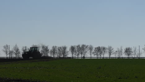 Silhouette-of-agricultural-tractor-with-tiller-in-field