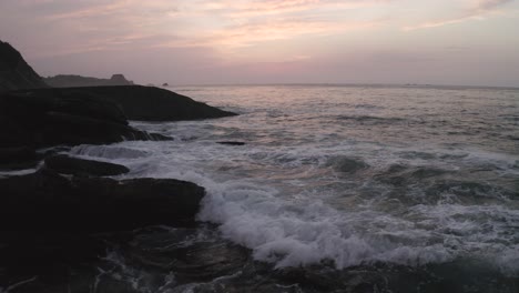 Aerial-drone-flying-at-low-altitude-over-ocean-waves-breaking-on-rocky-cliffs-at-sunset,-Pyrenees-Atlantiques,-France