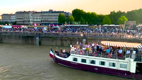 River-cruise-boat-during-Wine-Fair-with-French-flag-in-the-stern,-Aerial-dolly-out-shot