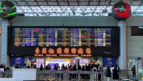 Airport-departure-hall-with-passengers-and-a-large-flight-information-display-board