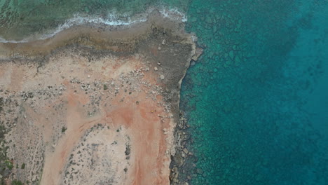 Aerial-view-of-the-rugged-coastline-with-crystal-clear-turquoise-waters,-golden-sandy-beaches,-and-lush-greenery-under-a-clear-blue-sky