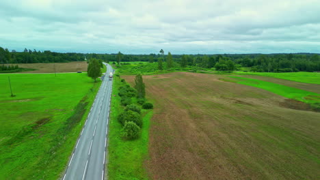 Aerial-view-of-a-field-with-an-asphalt-road-turning-at-the-end-to-forest-and-dead-grass-in-fields