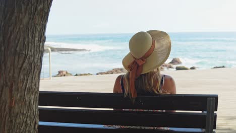 Mujer-Con-Sombrero-Para-El-Sol-Disfrutando-De-Vistas-Al-Mar-En-Un-Banco