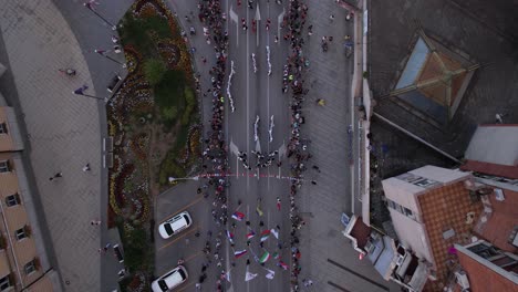 Aerial-View-of-Kids-Dancing-on-Street-in-Traditional-Constumes-With-Waving-Flags,-Licidersko-Srce-Children's-Folklore-Festival-in-Uzice,-Serbia