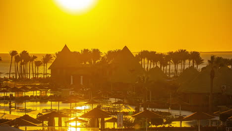 Beautiful-backlit-sunrise-on-the-beach-in-a-hotel-with-umbrellas,-palms-and-nature