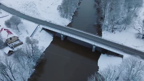 Abava-river-bridge-near-Renda-village-,-snow-covered-landscape,-aerial-view,-birdseye-orbit-shot
