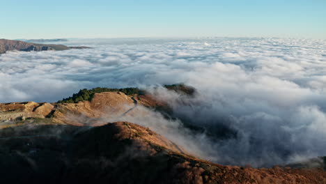 Majestuosa-Vista-Aérea-De-Un-Mar-De-Nubes-Sobre-Picos-Montañosos-Al-Amanecer,-Sereno-Y-Tranquilo