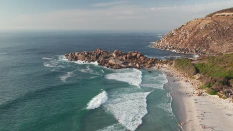 Cape-Town,-South-Africa---Tourists-Savoring-the-Frothy-White-Waves-During-Their-Vacation-at-Llandudno-Beach---Aerial-Drone-Shot