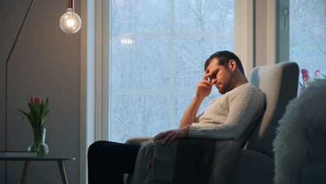 man-sits-in-recliner-with-his-hand-on-head