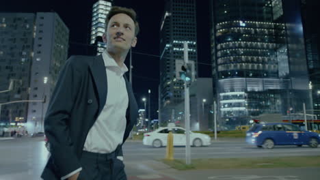 Smiling-young-business-man-in-suit-walking-in-big-metropolis-at-night