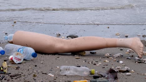 Solo-leg-broken-off-from-clothes-mannequin-and-other-plastic-trash-and-junk-drifted-ashore-polluting-a-beach-on-tropical-island