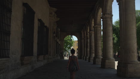 Offering-a-unique-viewpoint-of-Plaza-Vieja-adorned-with-arches,-a-tourist-can-be-seen-strolling,-appreciating-the-architectural-beauty