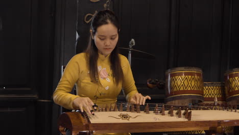 Vietnamese-Woman-in-Traditional-Costume-Performs-Music-Playing-on-Zheng-or-Guzheng,-Chinese-Plucked-Zither-at-Nha-Trang-Bay-Assembly-Hall