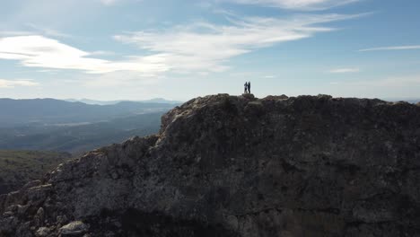 En-Este-Fascinante-Metraje-4k-Con-Dron,-Dos-Personas-Se-Encuentran-En-La-Cima-De-Una-Montaña,-Filmadas-Por-Un-Dron,-Mostrando-La-Impresionante-Belleza-Natural.