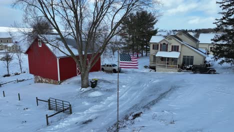 American-flag-waving-in-front-of-red-barn-and-house-in-rural-USA