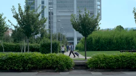 Business-People-Walking-Away-From-Modern-Office-Building-with-Green-Trees-and-Blue-Skies