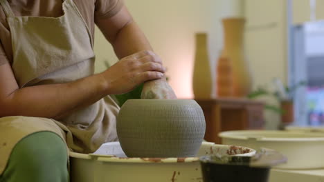 Male-potter-finishing-clay-flowerpot-spinning-on-pottery-turntable-close-up-in-workshop