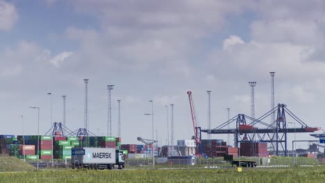 Distant-view-of-a-busy-cargo-port-with-stacked-containers-and-cranes,-a-Maersk-truck-in-foreground,-daylight