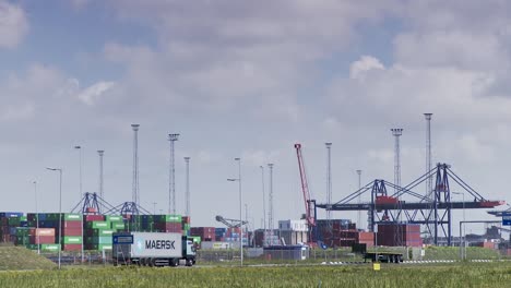 Vista-Lejana-De-Un-Concurrido-Puerto-De-Carga-Con-Contenedores-Apilados-Y-Grúas,-Un-Camión-Maersk-En-Primer-Plano,-Luz-Del-Día