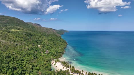 Aerial-flight-over-mountains-and-palm-tree-towards-La-Boca-del-Diablo-beach-on-a-sunny-day,-Dominican-Republic