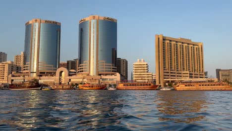 Dubai-Dos-Torres-Gemelas-Rascacielos-Emblemáticos-Edificios-En-Dubai-Creek-Riverside-Skyline-Un-Edificio-Con-Publicidad-Rolex-Emiratos-Árabes-Unidos,-Emiratos-Árabes-Unidos