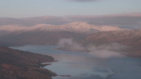 Static-shot-of-low-clouds-over-lake-Katrine-with-snowy-mountains-from-Ben-A'an