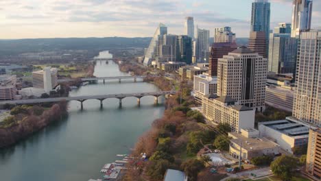 Toma-Aérea-De-Drones-Del-Hermoso-Distrito-Del-Centro-De-Austin,-Texas,-En-El-Río-Colorado,-Con-Vista-A-Los-Icónicos-Edificios-De-Austin-En-La-Orilla-Del-Río-Durante-La-Puesta-De-Sol-En-El-Invierno