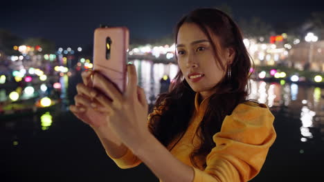 Schöne-Asiatische-Frau-Macht-Nächtliches-Selfie-Foto-Neben-Der-Flussspiegelung-In-Hoi-An,-Vietnam