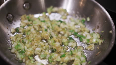 Sizzling-oil-around-medley-of-frying-onions,-garlic,-and-shallots-in-a-stainless-steel-pan