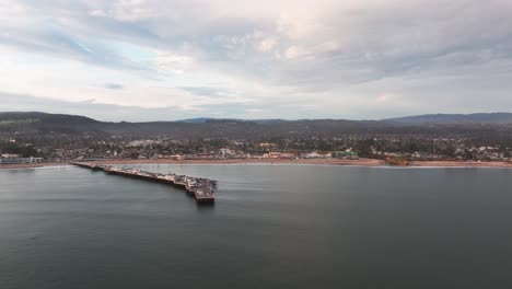 Disparo-Distante-De-Un-Dron-Panorámico-A-La-Derecha-Del-Muelle-De-Santa-Cruz-Y-La-Playa-Durante-La-Puesta-De-Sol