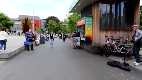 Einsamer-Musiker-Tritt-Auf-Dem-Eyre-Square-In-Galway-Auf,-Passanten-In-Der-Ferne