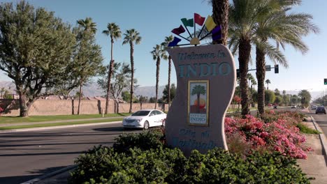 Bienvenido-A-Indio,-California,-Cartel-De-La-Ciudad-De-Los-Festivales-Con-Vehículos-Pasando-Y-Filmación-De-Video-Estable