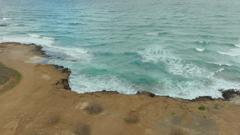 Aerial-view-of-a-rocky-shoreline-being-washed-by-turquoise-waves-of-the-Mediterranean-Sea