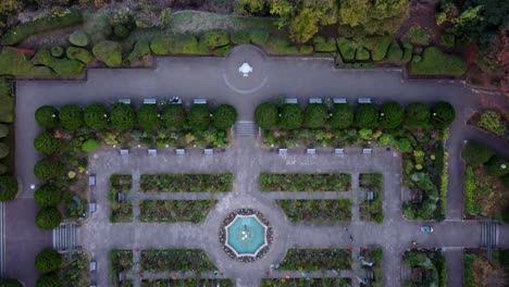 A-formal-garden-with-symmetrical-design-and-parked-cars,-at-dusk,-aerial-view