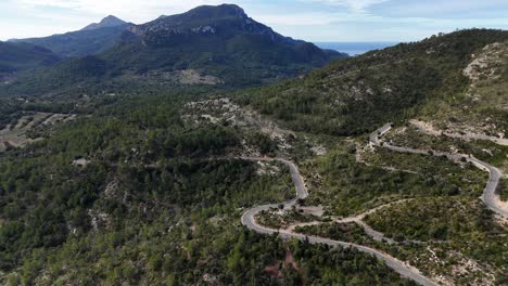 Kurvenreiche-Straße-Durch-Grüne-Hügel-Unter-Klarem-Himmel-Auf-Mallorca,-Luftaufnahme