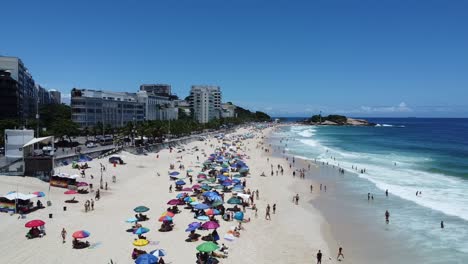 Toma-Lateral-Con-Drones-Volando-Bajo-En-La-Playa-De-Ipanema-Con-La-Playa-De-Arpoador-Al-Fondo,-Hermosas-Olas-Y-Cielo-Azul-En-Un-Día-Soleado