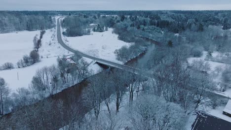 Snowy-landscape-with-Abava-river-near-Renda-village-during-winter,-aerial-view,-moving-forward,-tilt-down