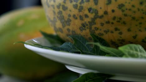 Close-up-of-spots-on-a-ripe-papaya-spinning-on-a-plate-with-green-leaves-on-it-vegan-vegetarian