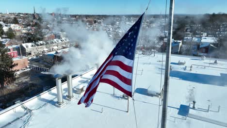 Smoking-chimneys-on-top-of-roof-with-waving-american-flag-in-american-town