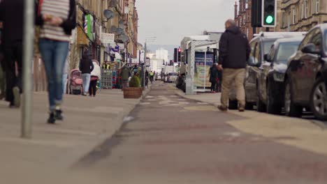 An-energetic-Victoria-Road,-people-walking-in-and-out-of-businesses---Glasgow-city-center-in-the-background