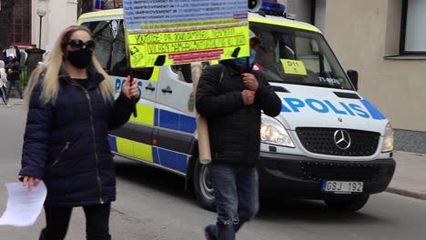 Masked-Covid-protesters-walk-by-Police-van-at-demonstration,-Stockholm