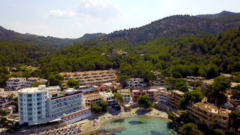 Approaching-drone-shot-slowly-tilting-down-to-show-the-beachfront-of-Playa-Lletas,-a-secluded-resort-in-the-Mediterranean-island-of-Mallorca-in-Spain