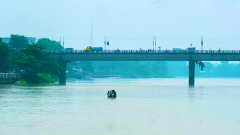 Boat-Sailing-In-The-Surma-River-With-Vehicles-Driving-On-The-Road-Bridge-In-Bangladesh